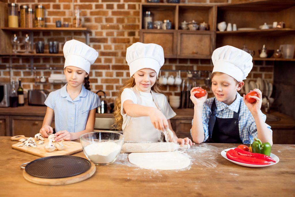 children making pizza dough and preparing pizza ingredients in kitchen