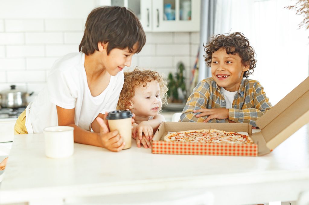 Children real siblings eating pizza together at home