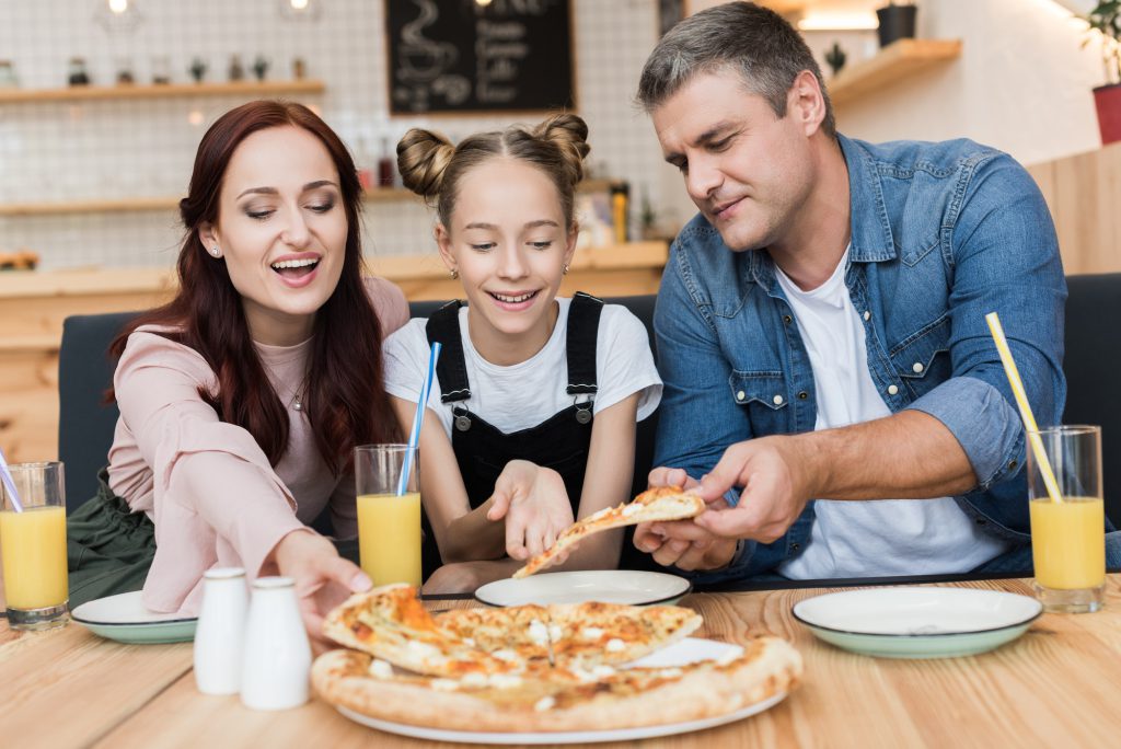 happy family with teen daughter eating pizza in cafe